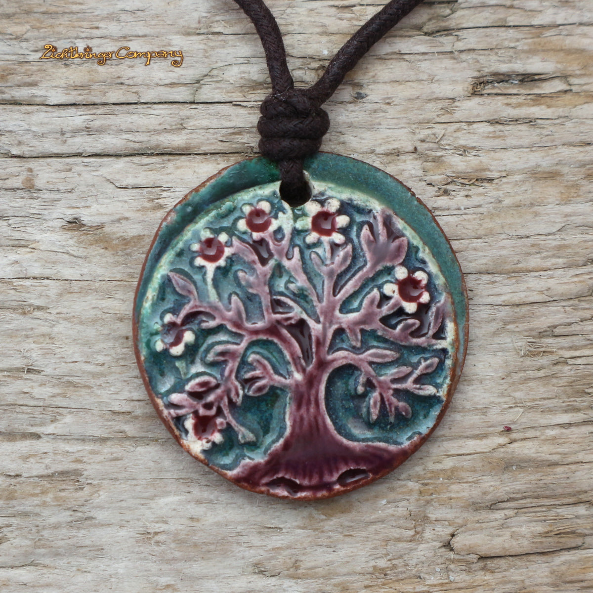 Lebensbaum-Anhänger aus Ton in Dunkelgrün, an gewachster Baumwollkette – handgefertigtes Keramik-Amulett. Brauner Baum, grüner Hintergrund.